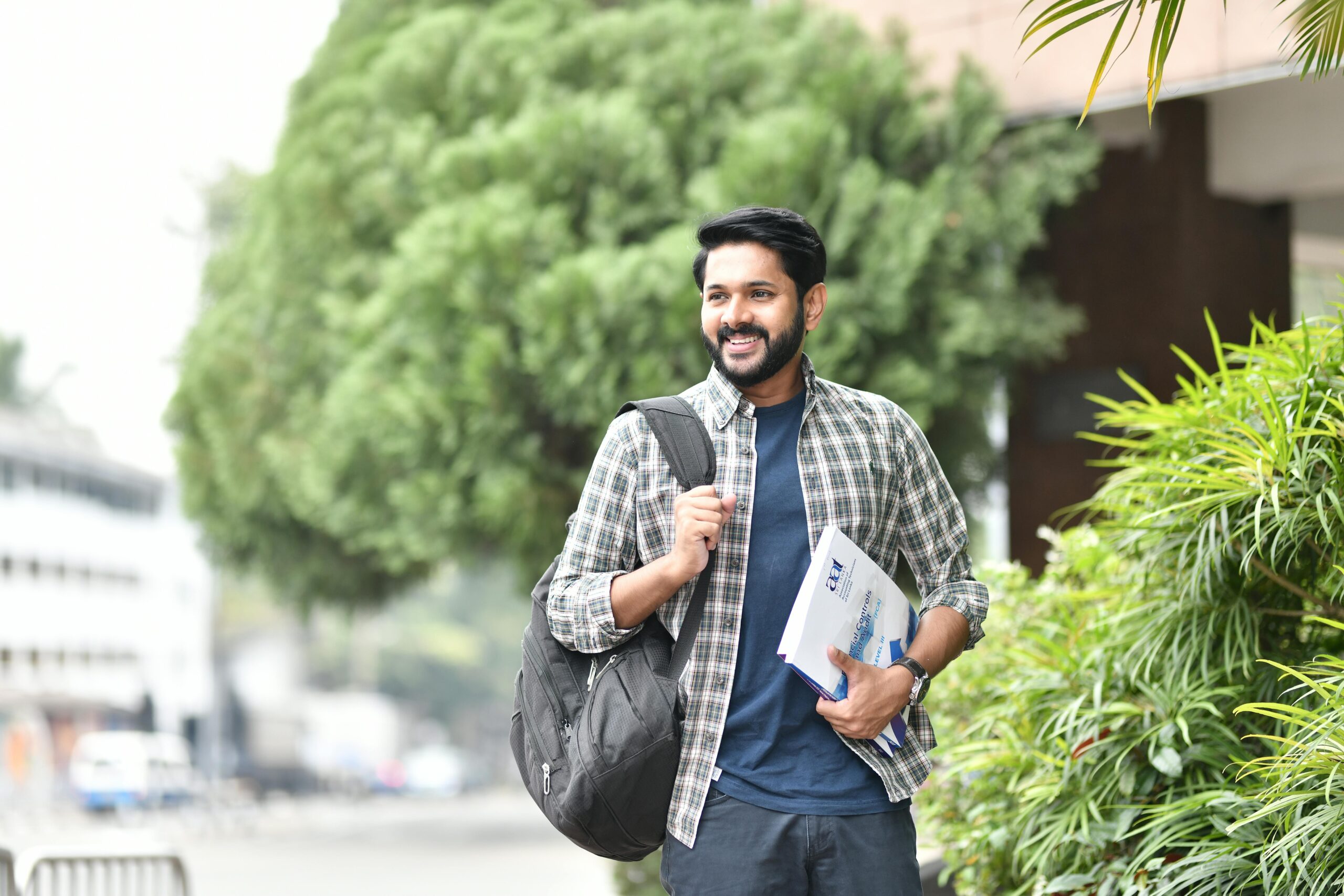 Young man smiling outdoors with backpack and books. Casual, candid, and vibrant student life moment.